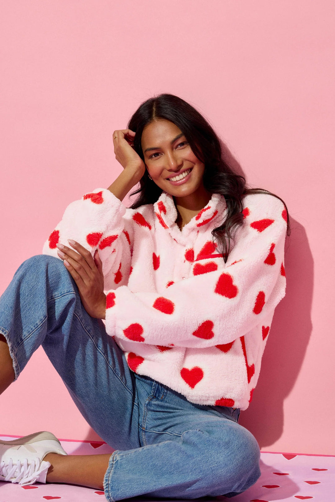 Woman wearing a pink hoodie with red heart patterns on a pink background