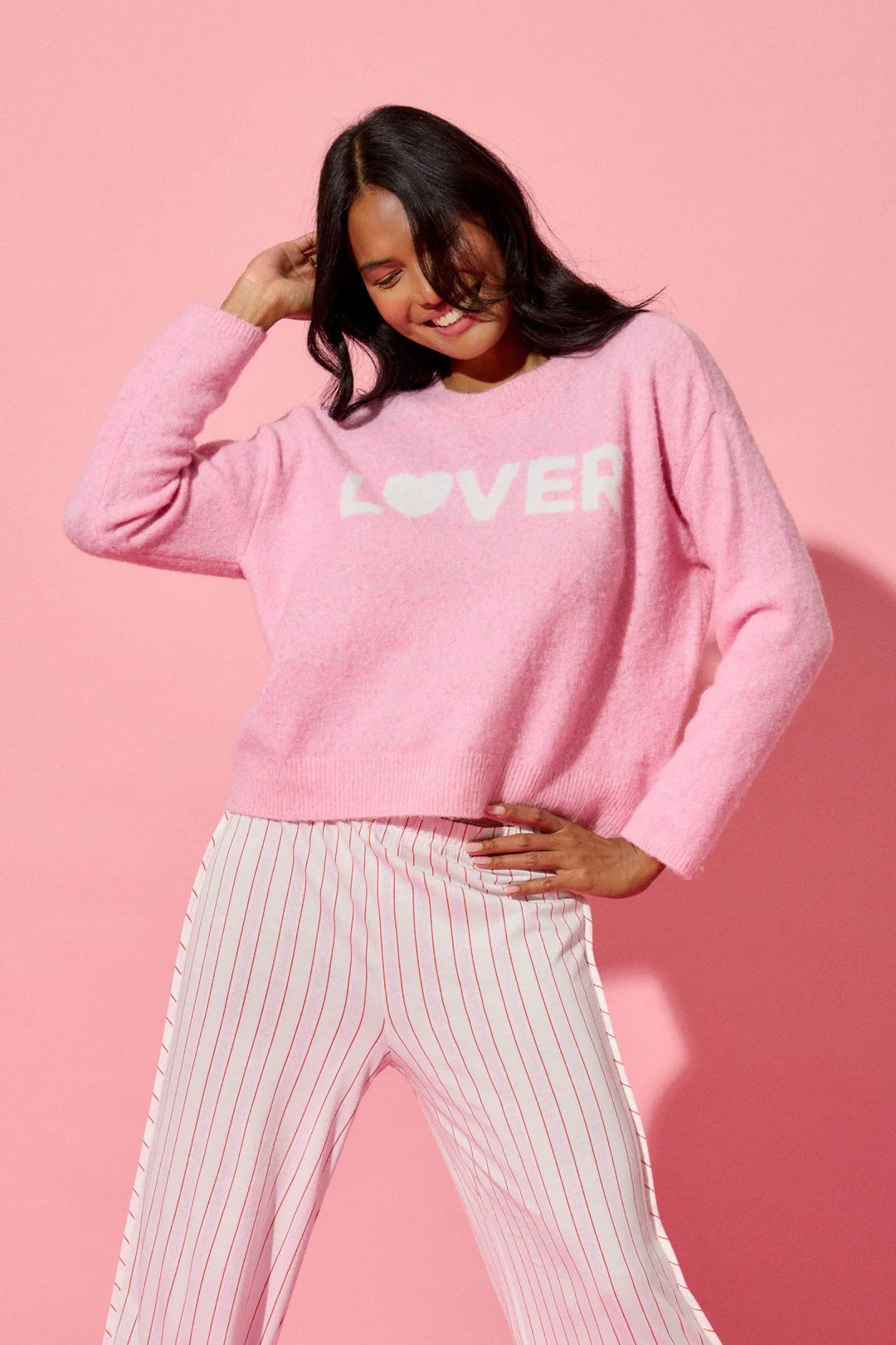 Person wearing a pink sweatshirt with 'LOVER' printed on it against a pink background