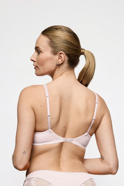 A woman shown from the back wearing a light pink lace-trim lingerie set against a plain light gray studio background.