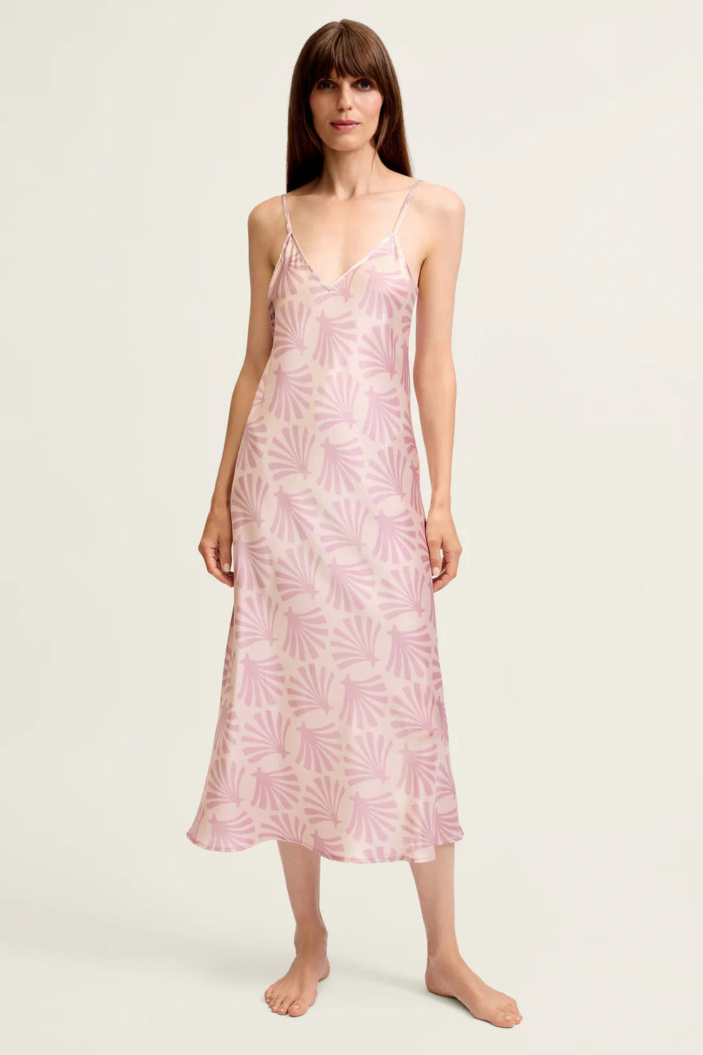 Woman wearing a pink floral silk slip dress on a white background