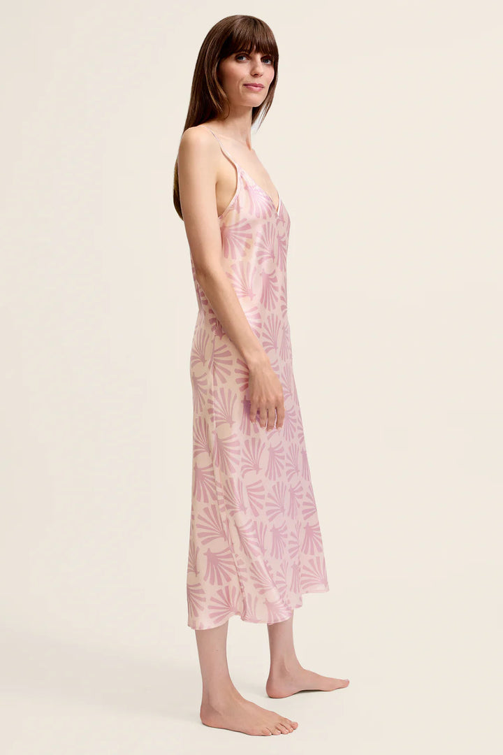 Woman wearing a pink printed silk slip dress with leaf pattern on a plain background