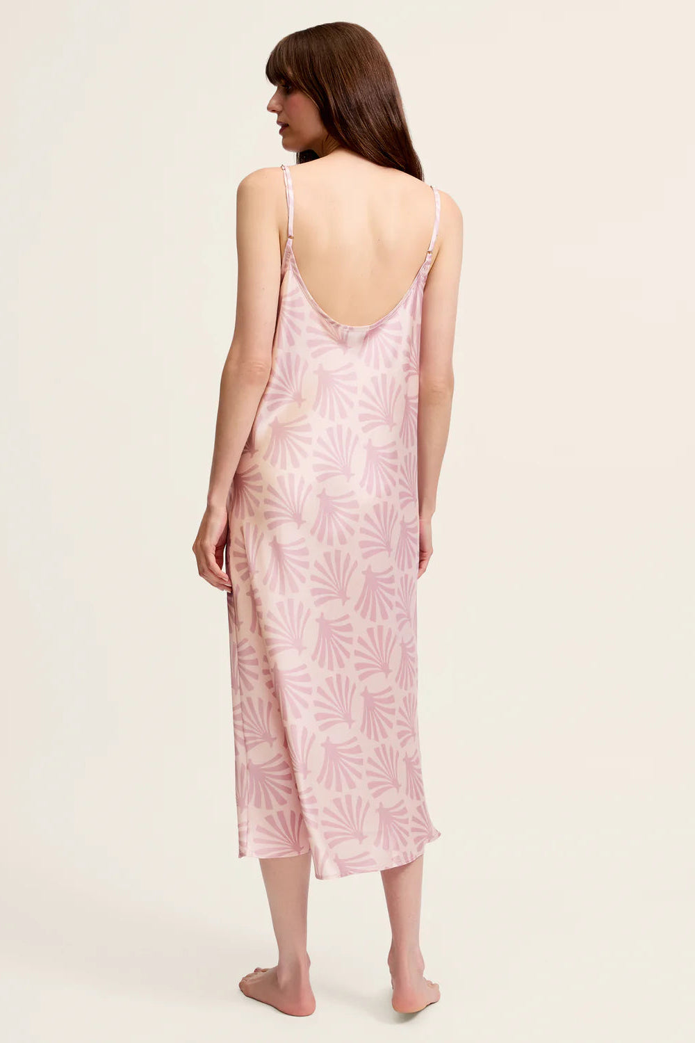 Woman wearing a pink floral slip dress on a plain background