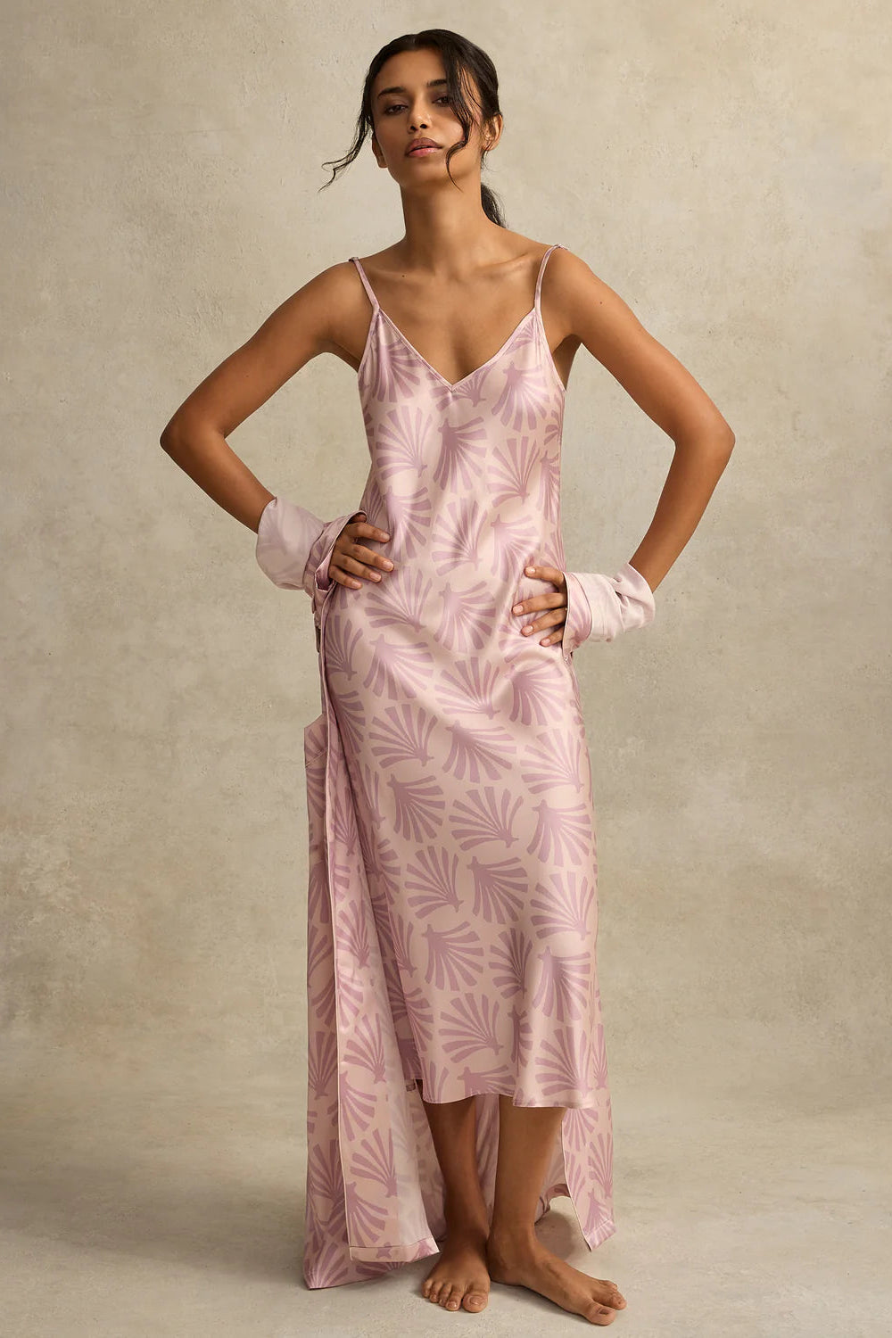 Woman wearing a pink silk nightgown slip dress with a subtle pattern against a neutral background
