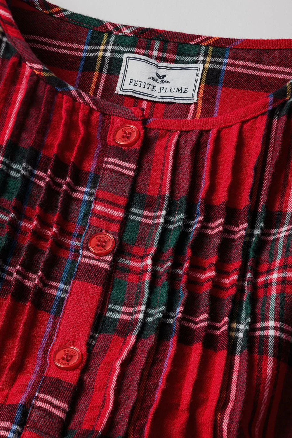 Red plaid shirt with 'Petite Plume' label on a gray background