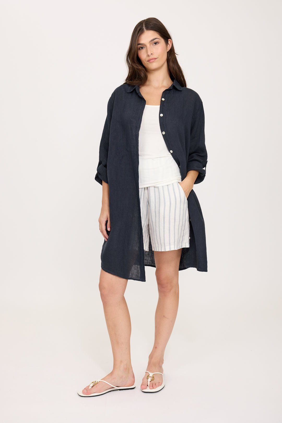 Woman wearing a navy long linen shirt over a white outfit on a white background