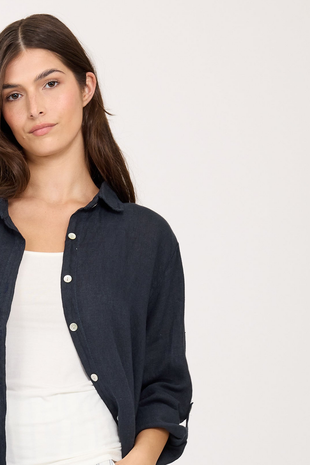 Woman wearing a navy blue linen button-up shirt over a white top on a plain background