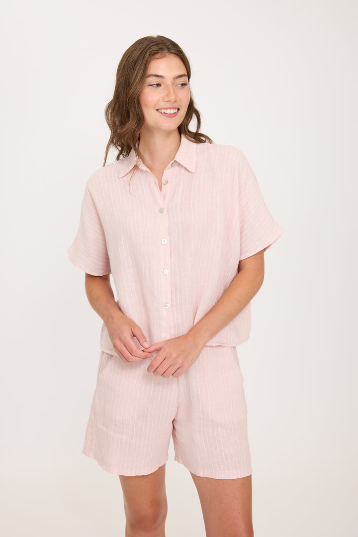 Woman wearing a light pink striped linen shirt and shorts set on a white background. Vacation outfit, perfect for summertime or hot weather.