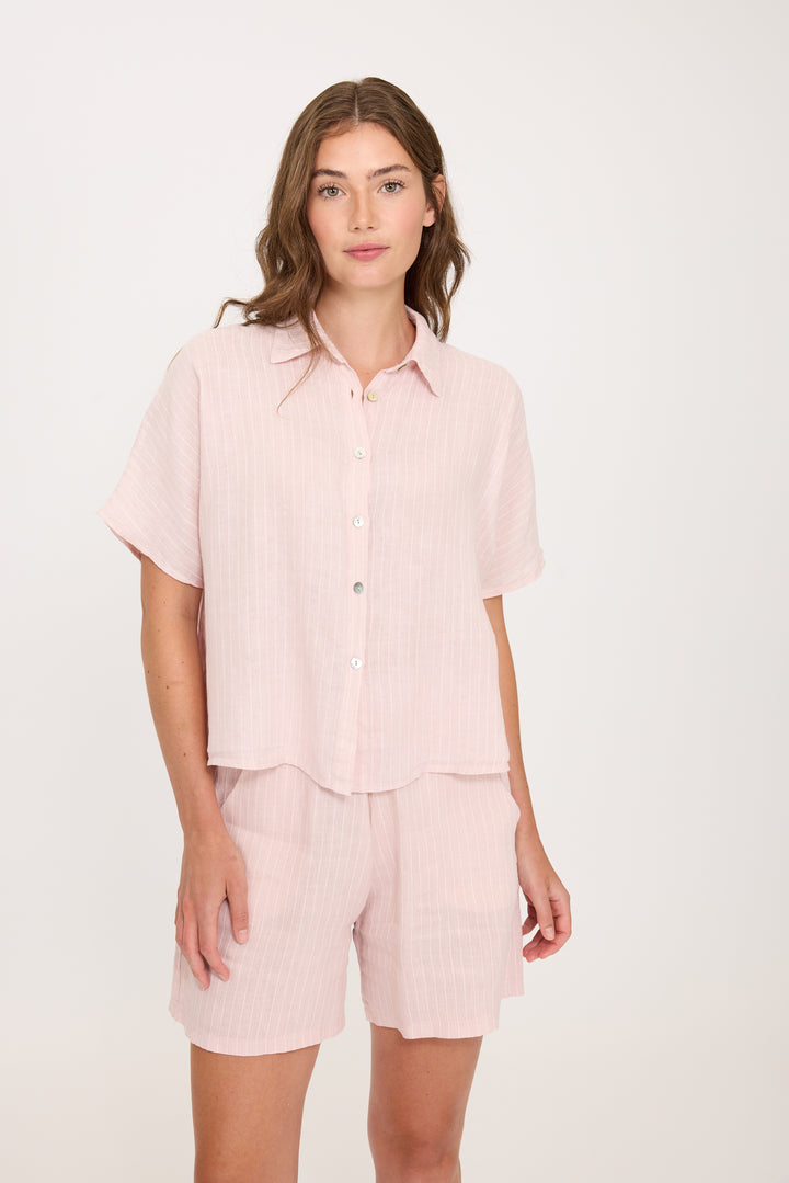 Woman wearing a light pink striped linen shirt and shorts set on a white background. Vacation outfit, perfect for summertime or hot weather.