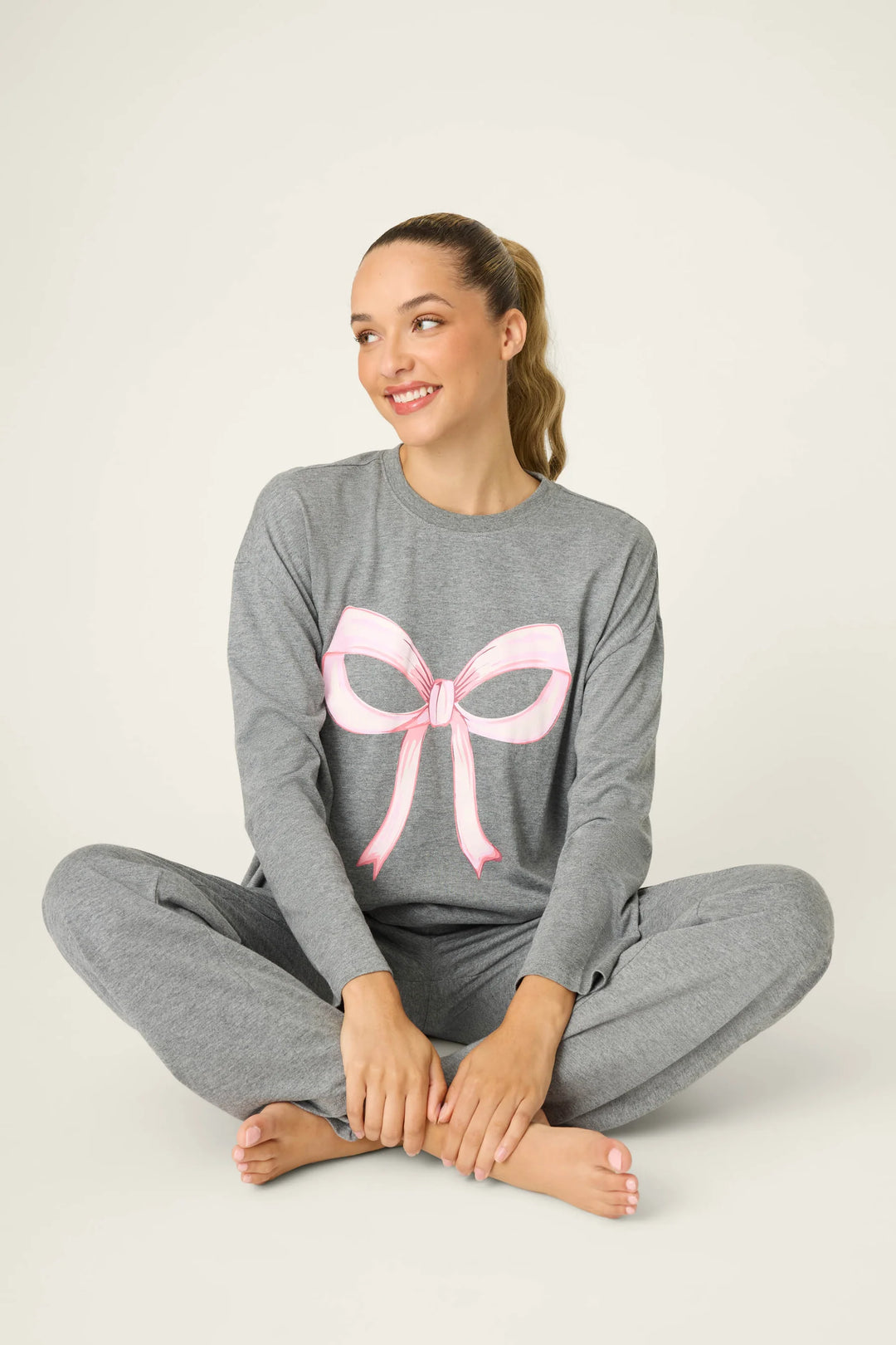 Woman wearing gray pajamas with a pink bow design on a white background
