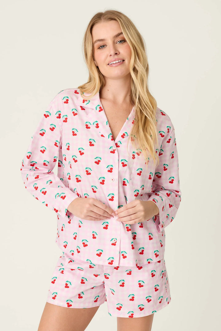 Woman wearing a pink pajama set with cherry pattern on a beige background