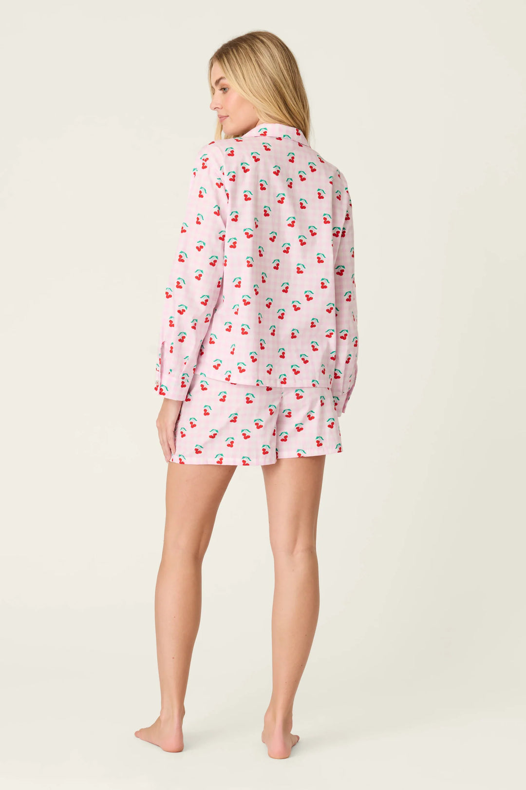 Woman wearing a pink pajama set with cherry pattern on a white background