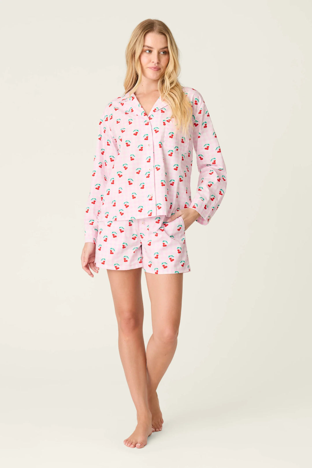 Woman wearing a pink pajama set with cherry pattern on a white background