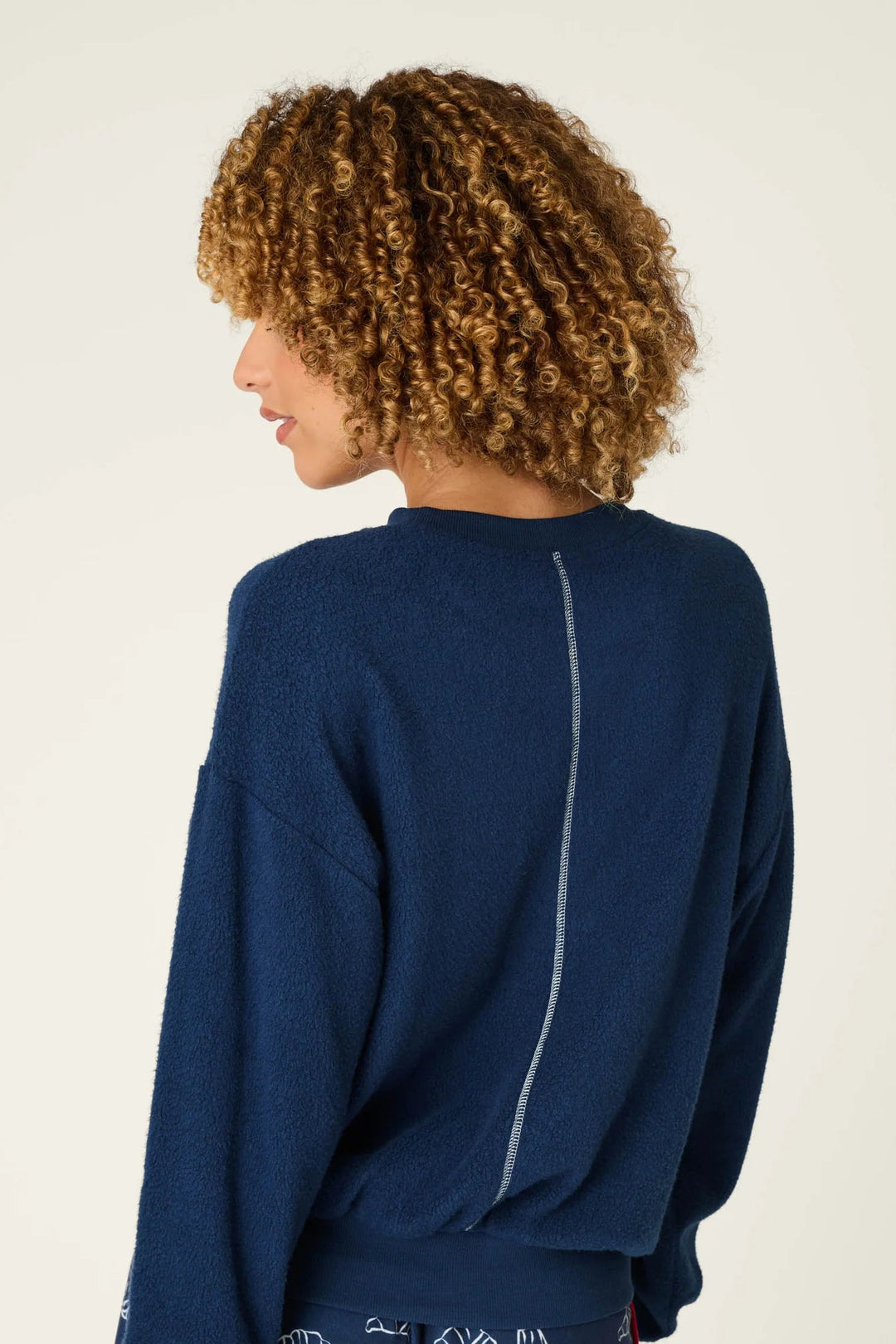 A model shown from the back wearing a navy blue crewneck sweatshirt and matching navy shorts with a white graphic pattern, against a plain off-white background.