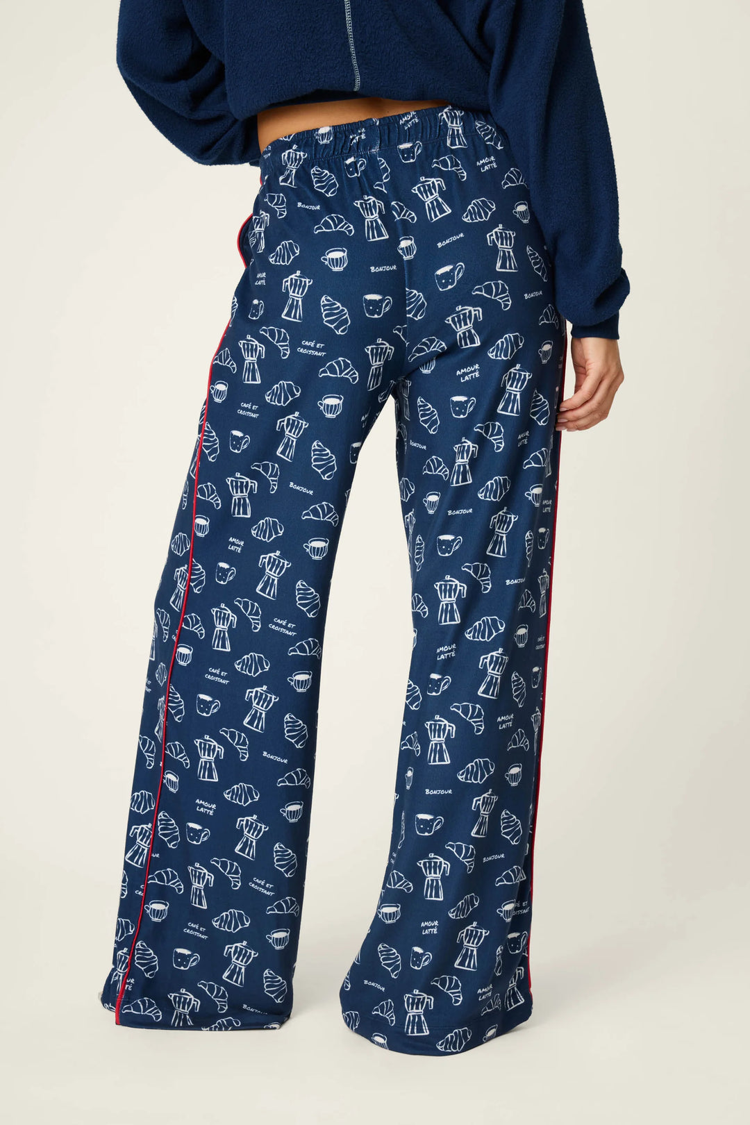 A person wearing navy wide-leg pants with an allover white pastry print and red side piping, paired with a navy cropped top, photographed against a light neutral studio background.