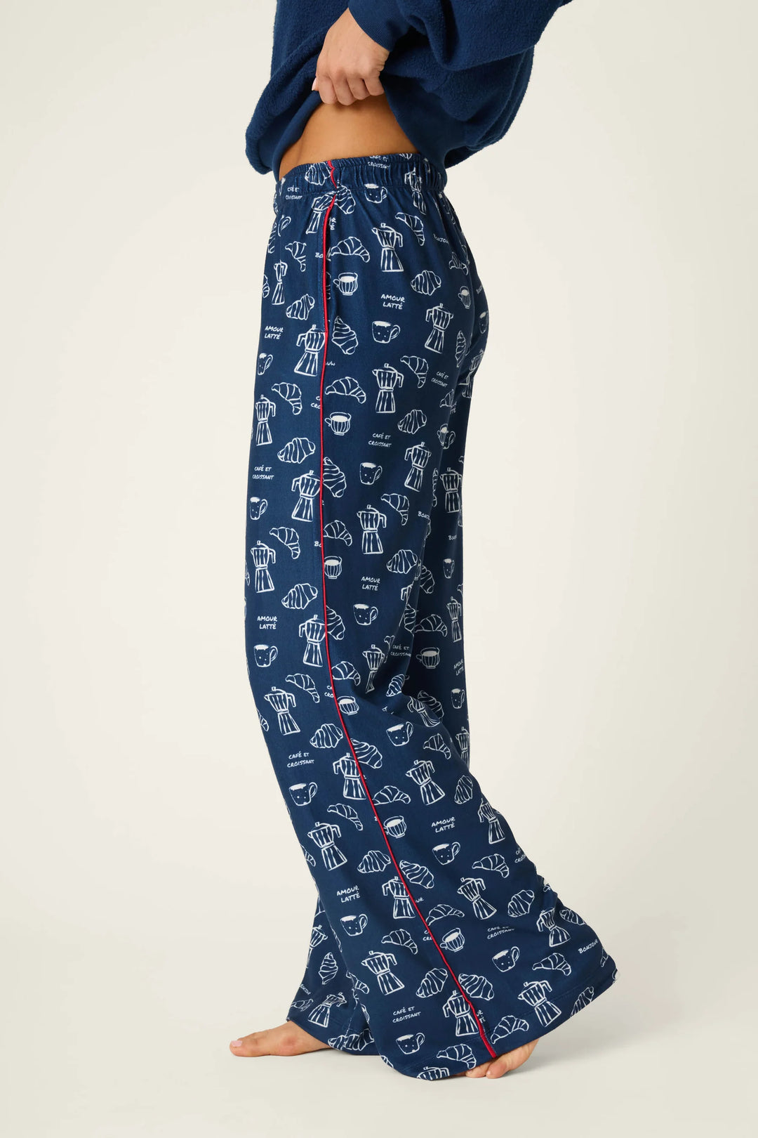 A person wearing navy blue pajama pants with a white line-art print of espresso cups and a red piping detail along the side, shown against a plain light background.