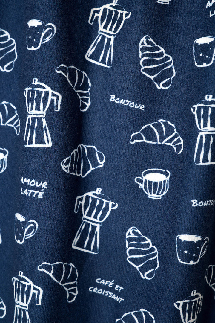 A close-up of a navy blue fabric with a white hand-drawn pattern of coffee mugs, croissants, and French text including 'BONJOUR', 'AMOUR LATTE', and 'CAFÉ ET CROISSANT'.