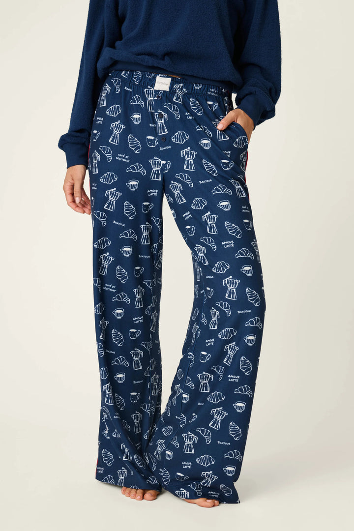A person wearing navy blue wide-leg pajama pants with a white allover print of coffee-themed illustrations, paired with a navy long-sleeve top, against a plain light background.