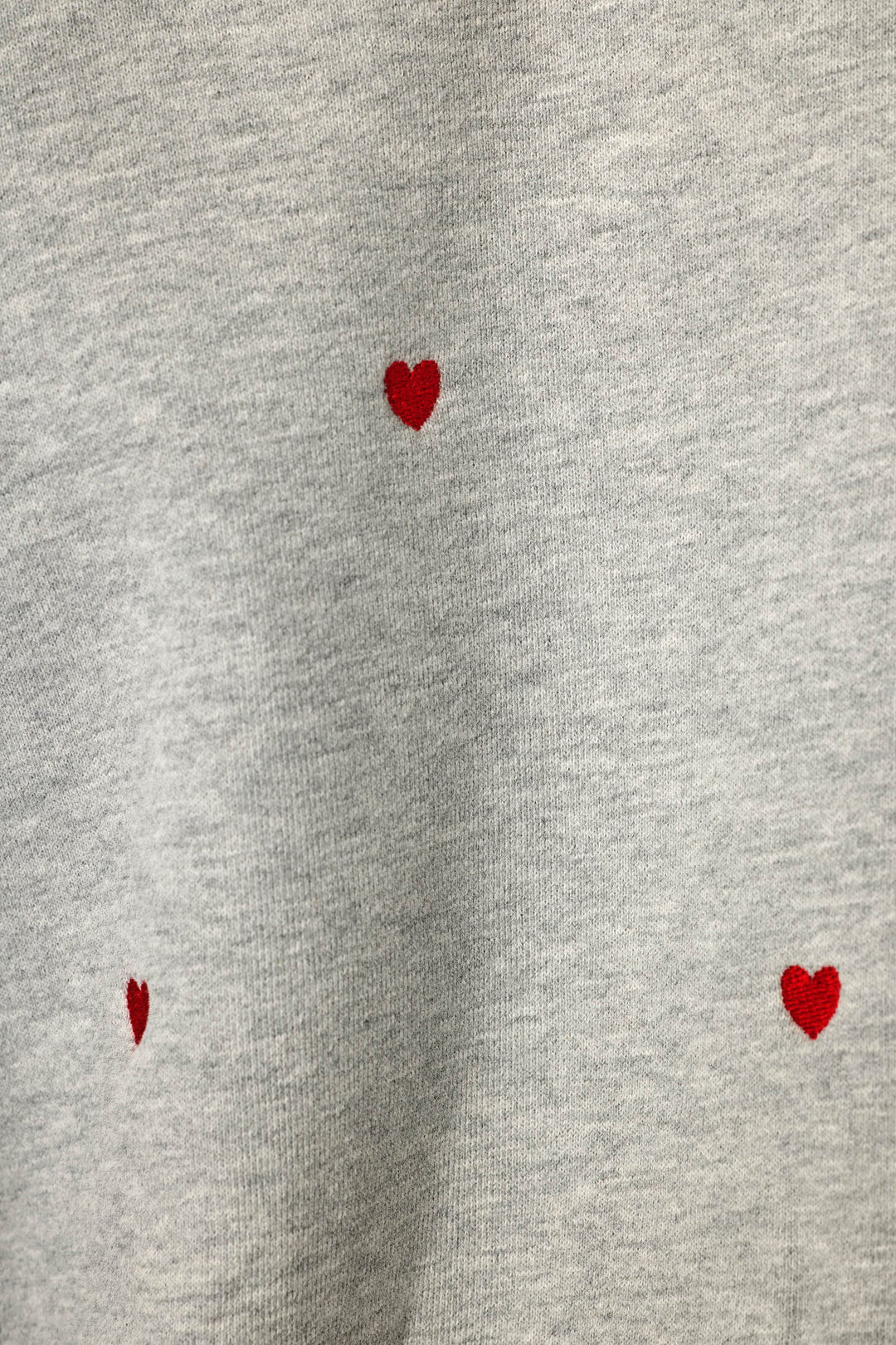 Close-up of a light heather gray fabric with three small red heart motifs scattered across it.