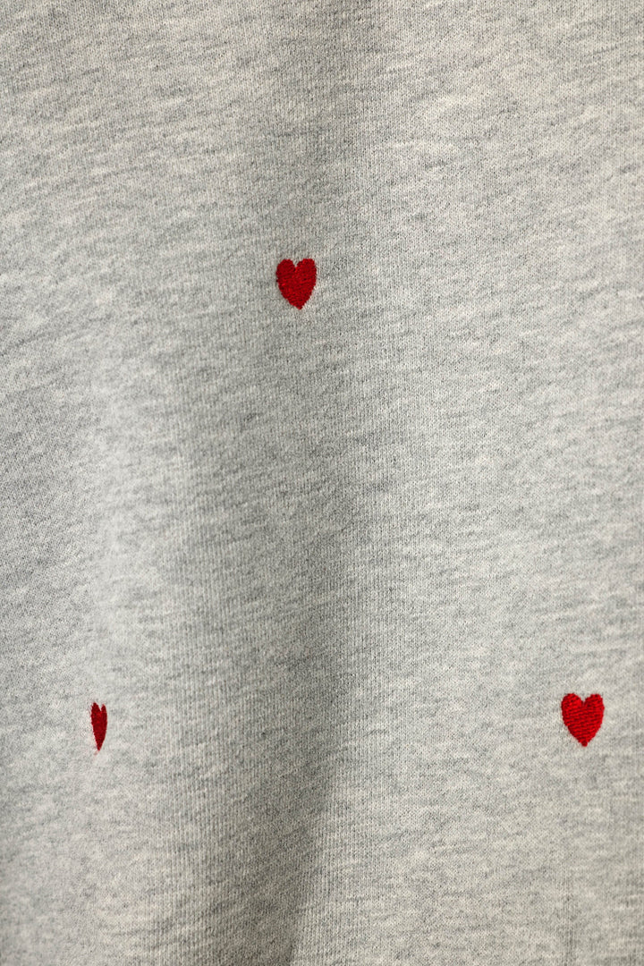 Close-up of a light heather gray fabric with three small red heart motifs scattered across it.