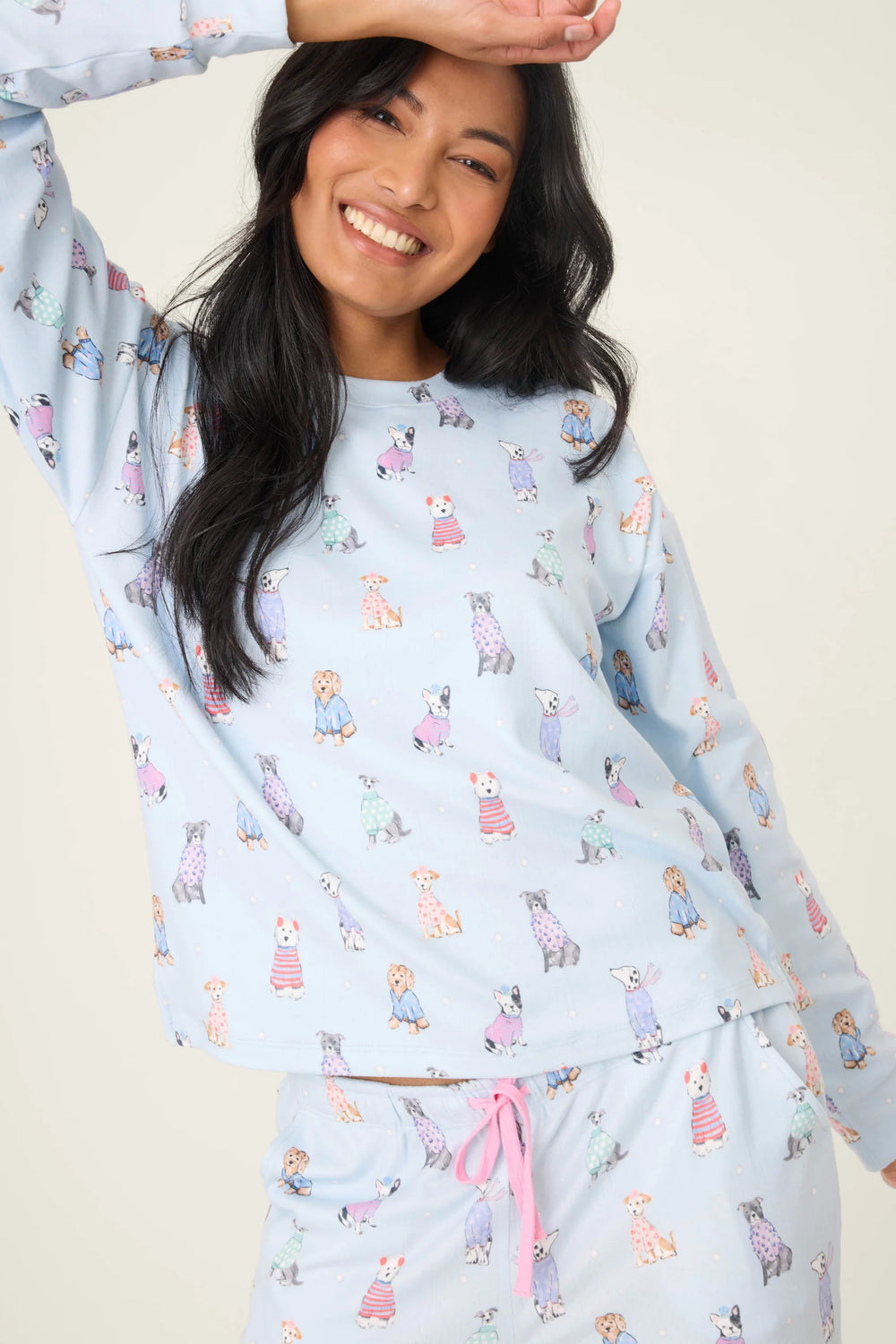 Woman wearing a light blue pajama set with dog print on a plain background
