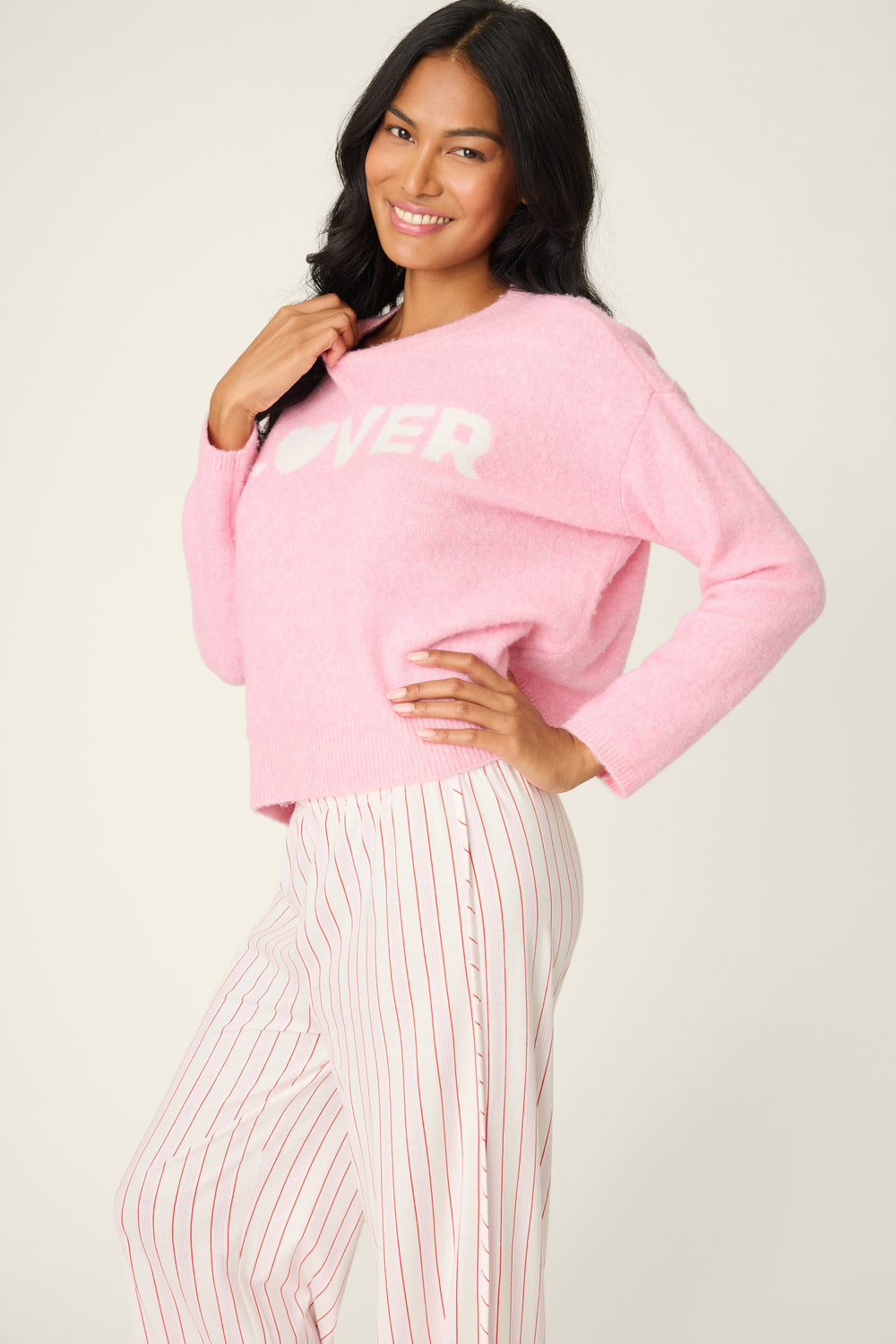 Woman wearing a pink sweater with text and white pants on a plain background
