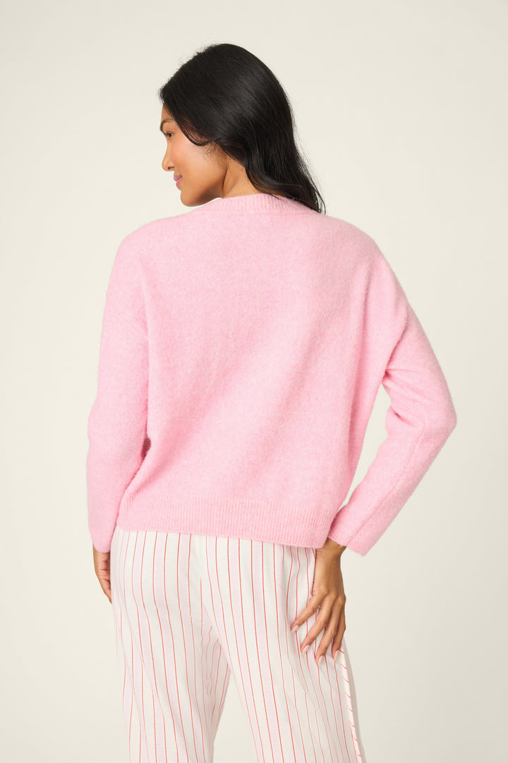 Woman wearing a pink sweater and striped pants on a plain background
