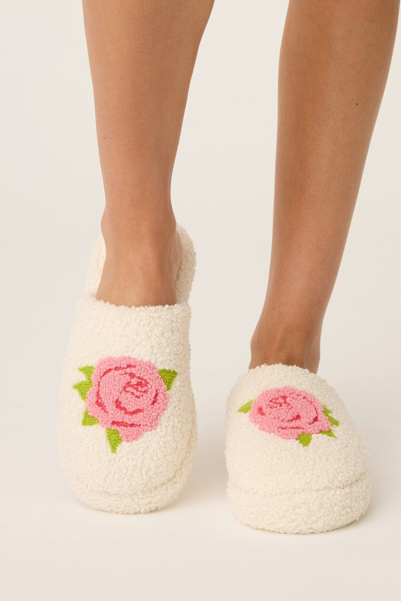 White slippers with pink floral rose designs worn by a person on a light background
