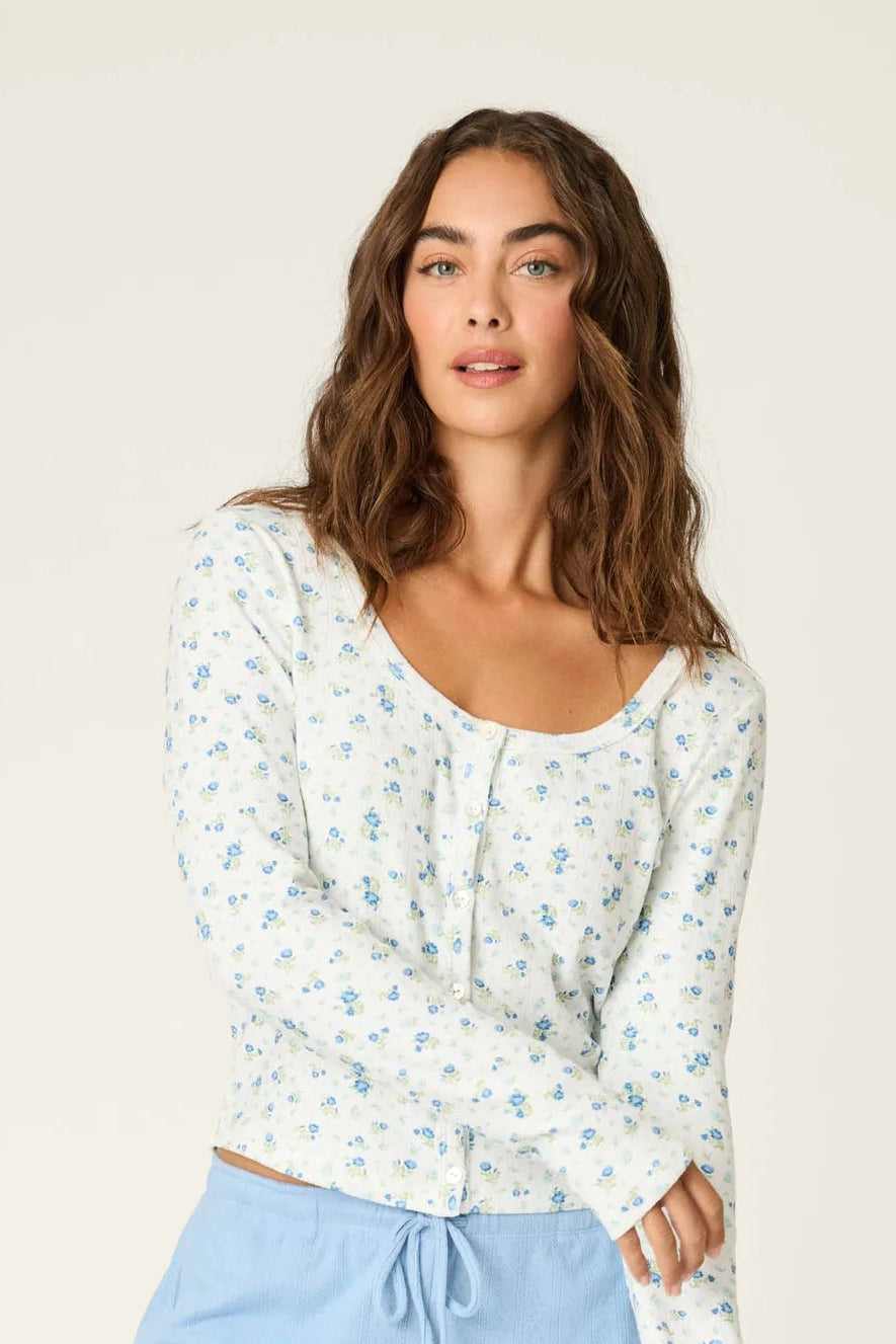 Woman wearing a white patterned long-sleeve top and light blue shorts on a beige background