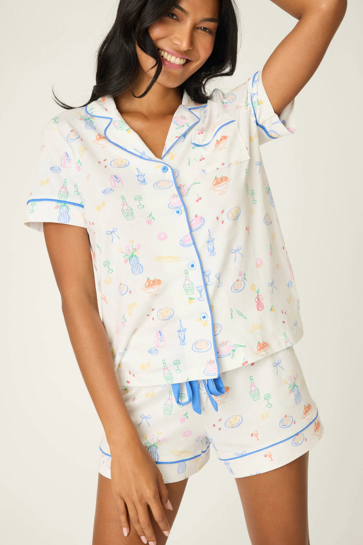 Woman wearing a colorful pajama set with breakfast designs on a plain background