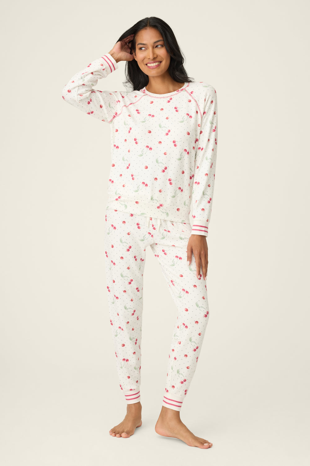 Woman wearing a white pajama set with red cherry pattern on a plain background