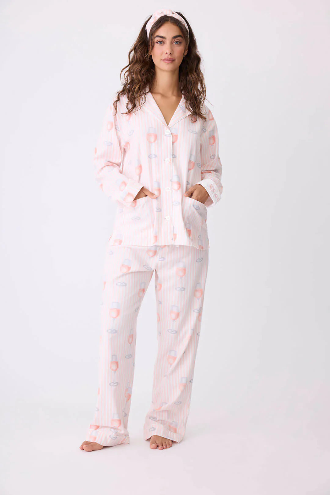 Woman wearing a pink and white patterned pajama set with wine glasses on a white background