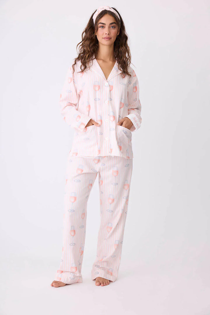 Woman wearing a pink and white patterned pajama set with wine glasses on a white background