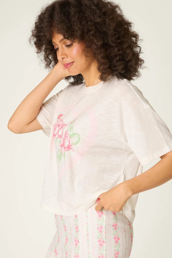 Woman wearing a white t-shirt with a rose print and pants with floral designs on a plain background