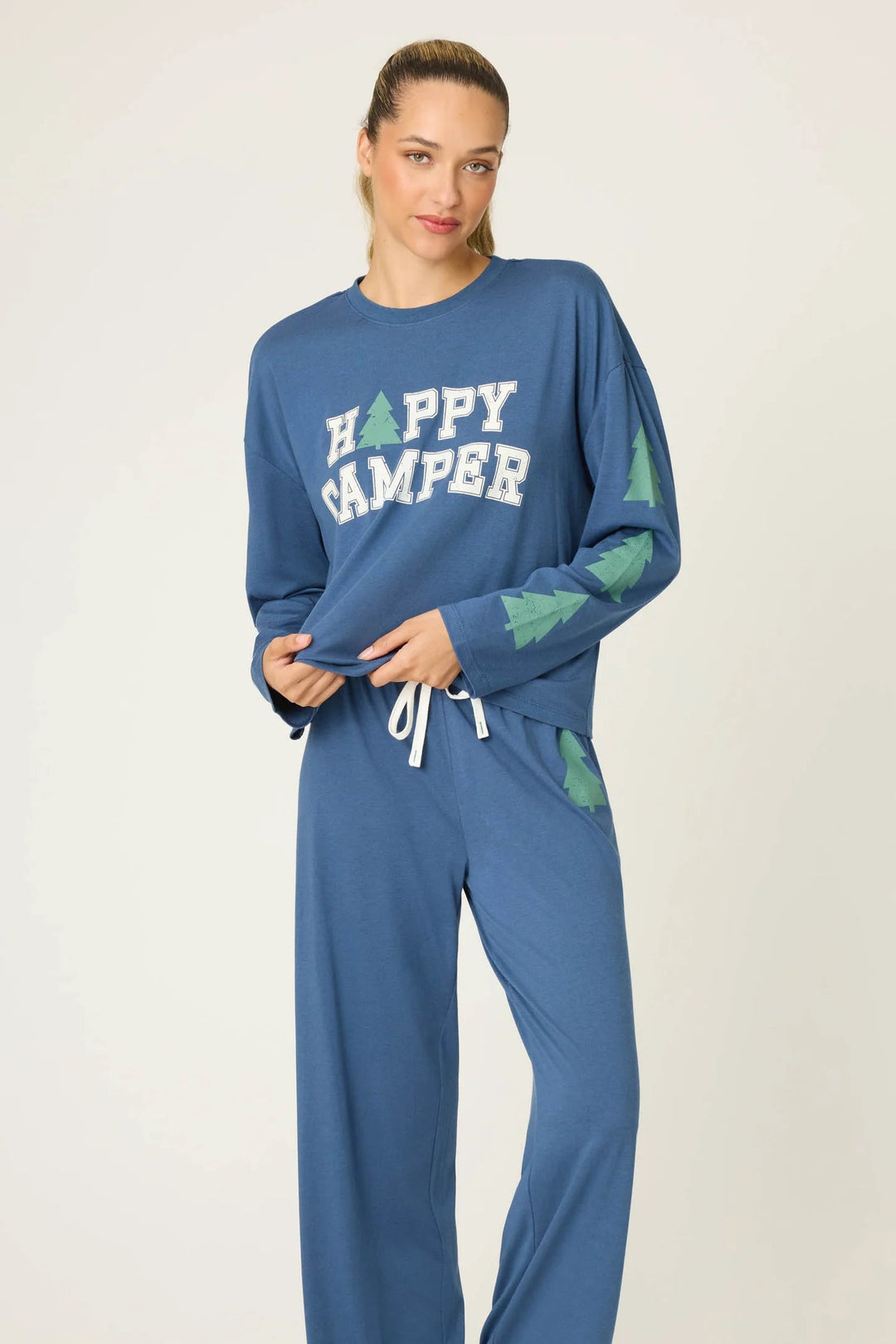 Woman wearing a blue 'Happy Camper' pajama set on a white background
