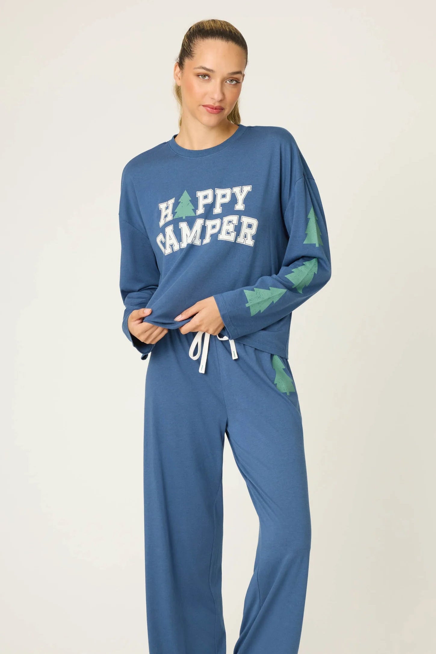 Woman wearing a blue 'Happy Camper' pajama set on a white background
