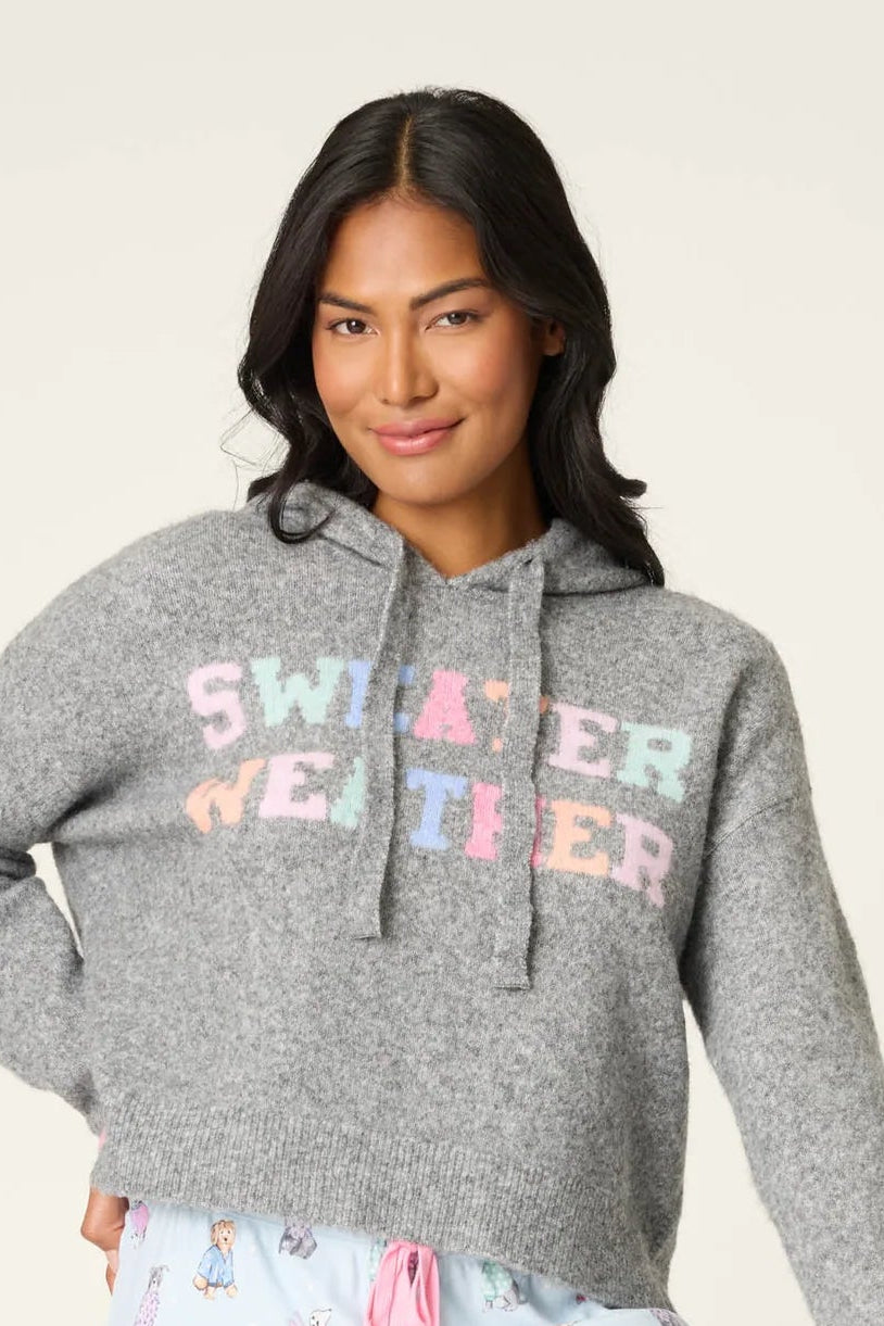 Woman wearing a gray hoodie with 'Sweater Weather' text and light blue shorts with pink floral pattern on a white background.