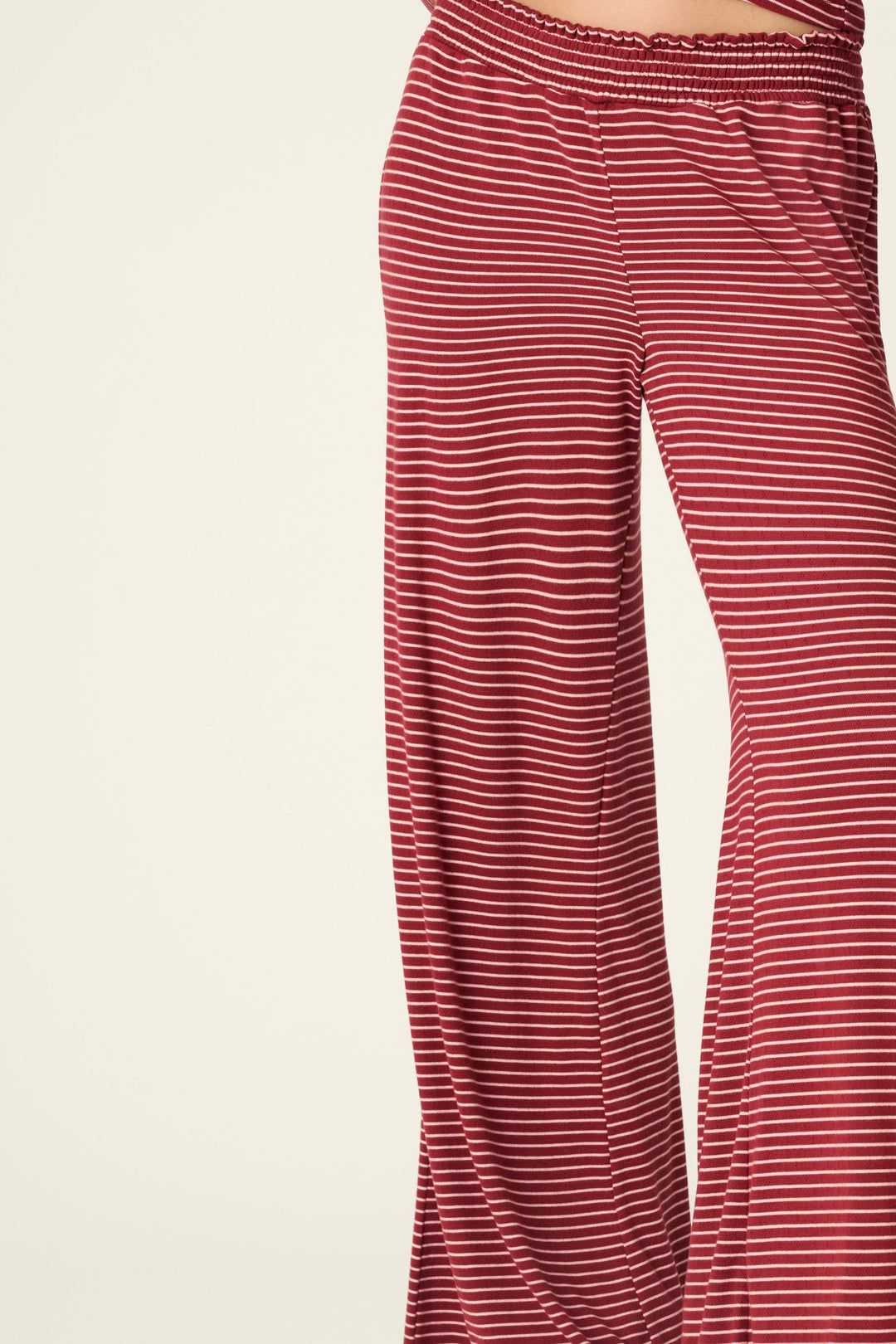 A model wearing a matching two-piece loungewear set consisting of a long-sleeve top and wide-leg pants, both in a red and white horizontal stripe pattern, against a plain light beige background.