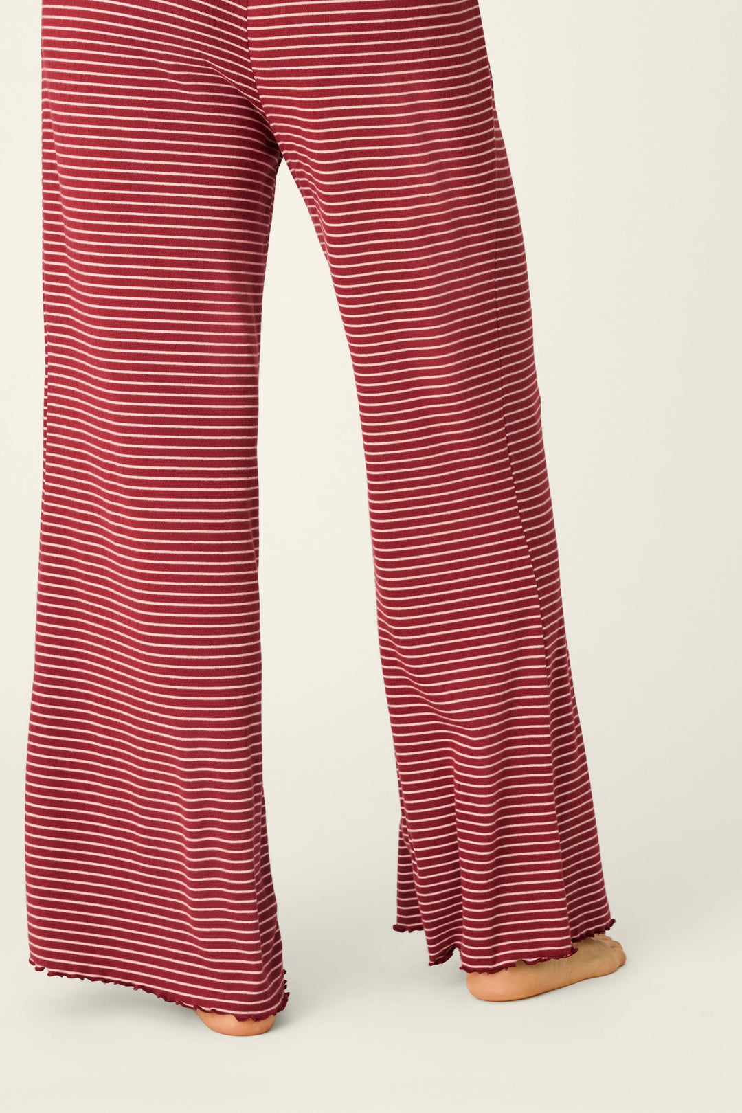 A person shown from the back wearing a matching long-sleeve top and wide-leg pants set with thin horizontal red and white stripes, photographed against a plain light beige studio background.