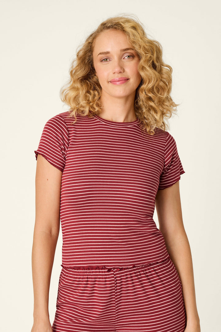 A woman with curly blonde hair wearing a matching two-piece loungewear set consisting of a short-sleeve t-shirt and shorts, both featuring a red and white horizontal stripe pattern, against a plain off-white background.