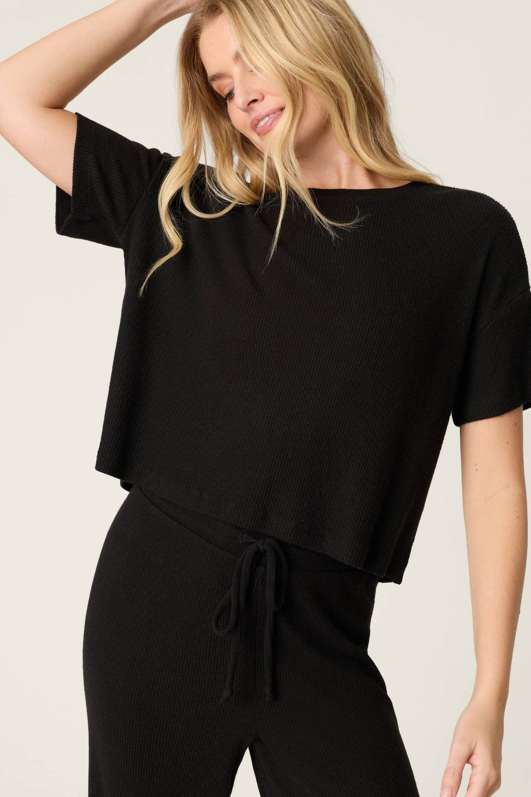 Woman wearing a black outfit with a tie detail on a plain background