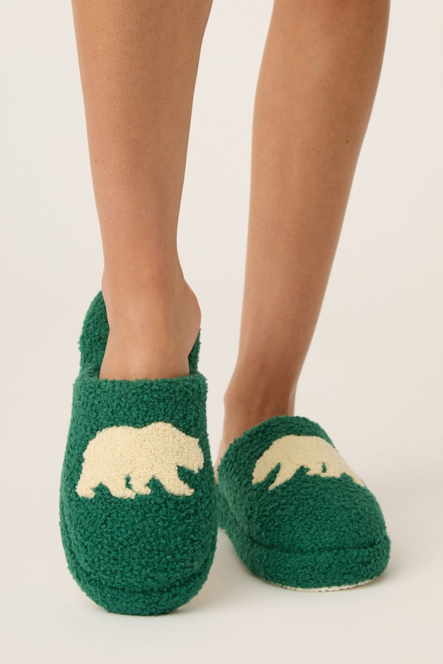 Green slippers with bear design worn by a person on a light background