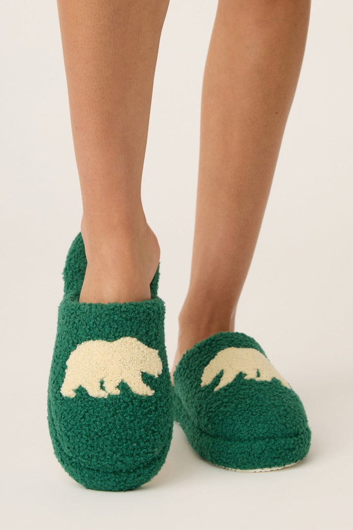 Green slippers with bear design worn by a person on a light background