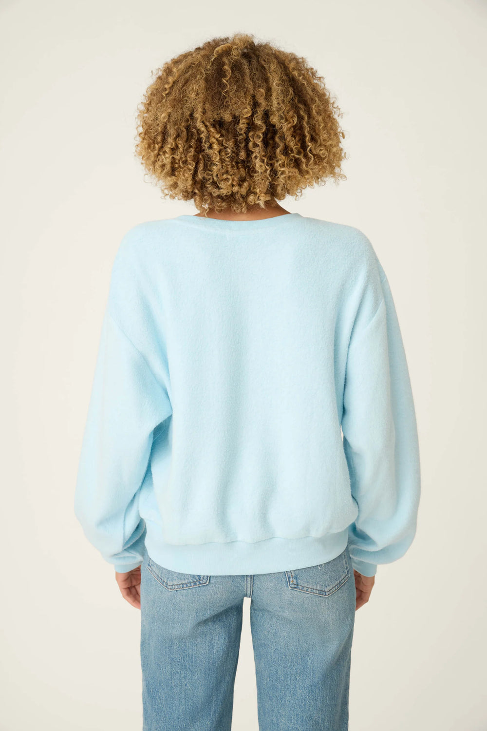 Person wearing a light blue sweatshirt and jeans on a plain background
