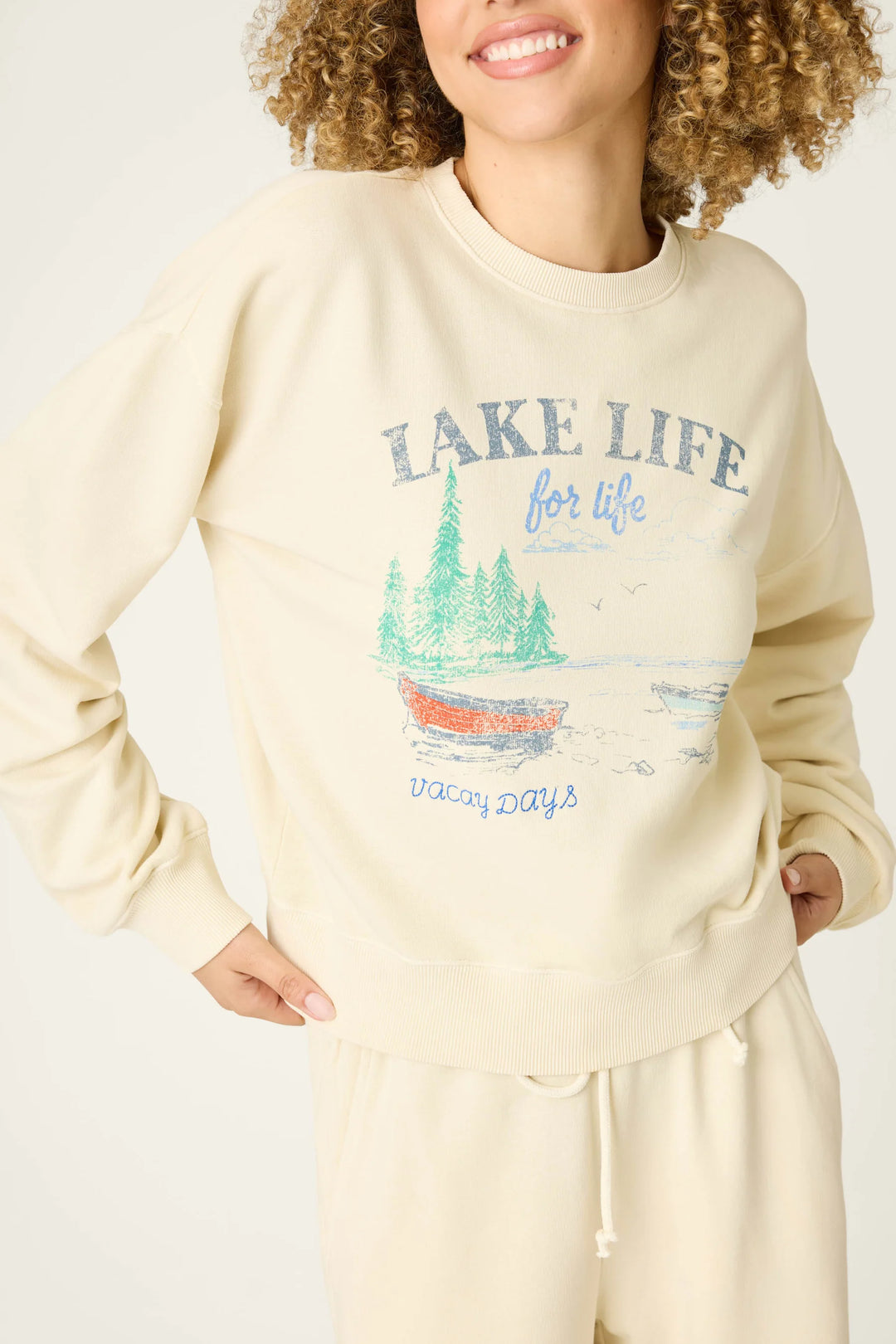Person wearing a cream sweatshirt with 'Lake Life' graphic design on a plain background