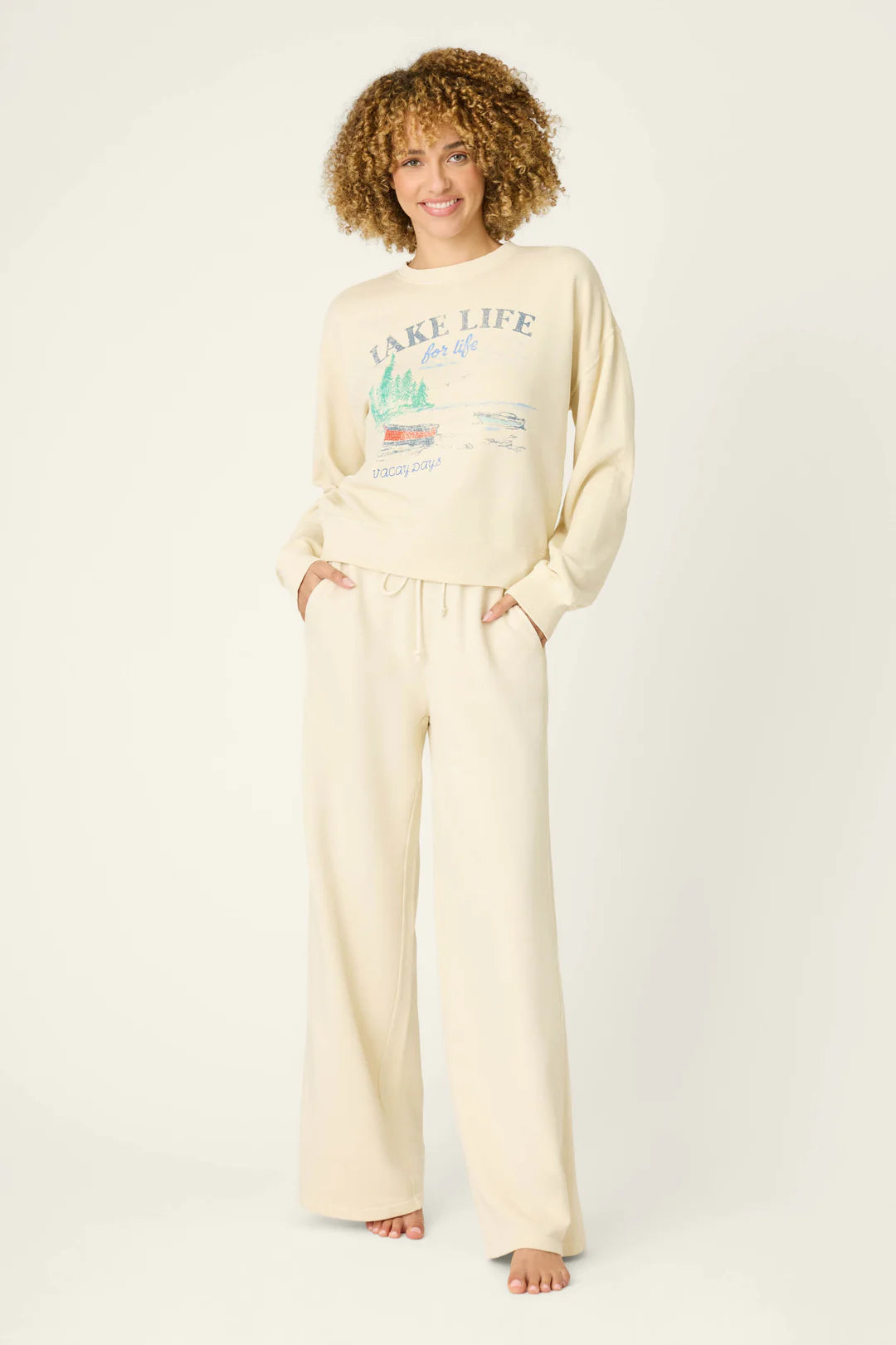 Woman wearing a cream-colored 'Lake Life' sweatshirt and pants on a white background