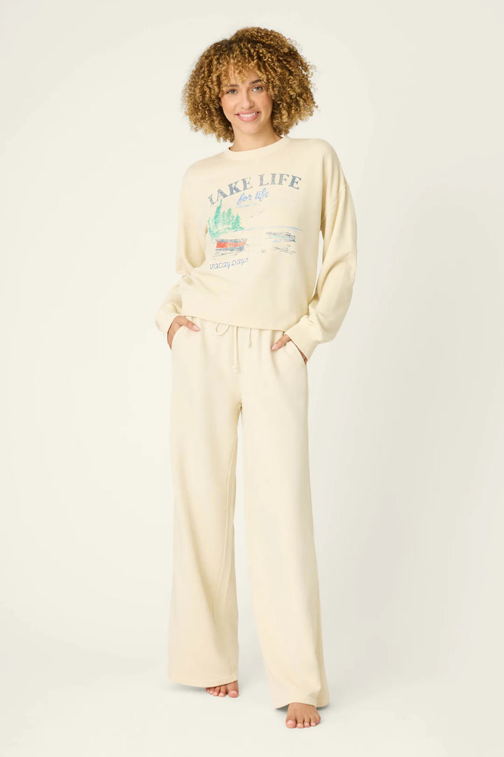 Woman wearing a cream-colored 'Lake Life' sweatshirt and pants on a white background