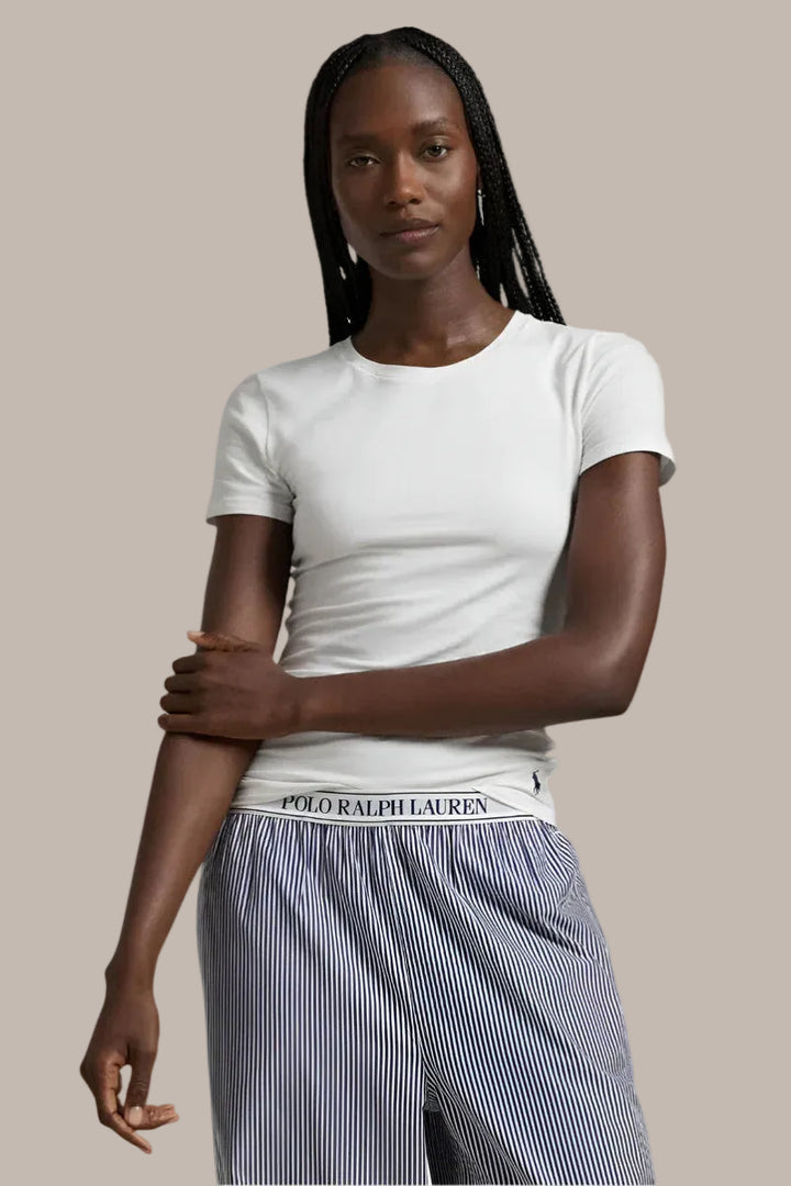 Woman wearing a white polo ralph lauren t-shirt and striped pants with a visible pony brand logo on a light gray background