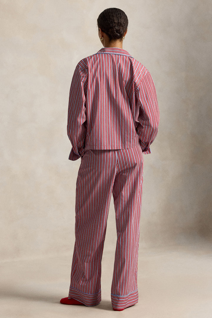 woman wearing a red blue striped pajama set with blue piping trim. Buttoned top with notch collar and full length pant with elastic waistband. 