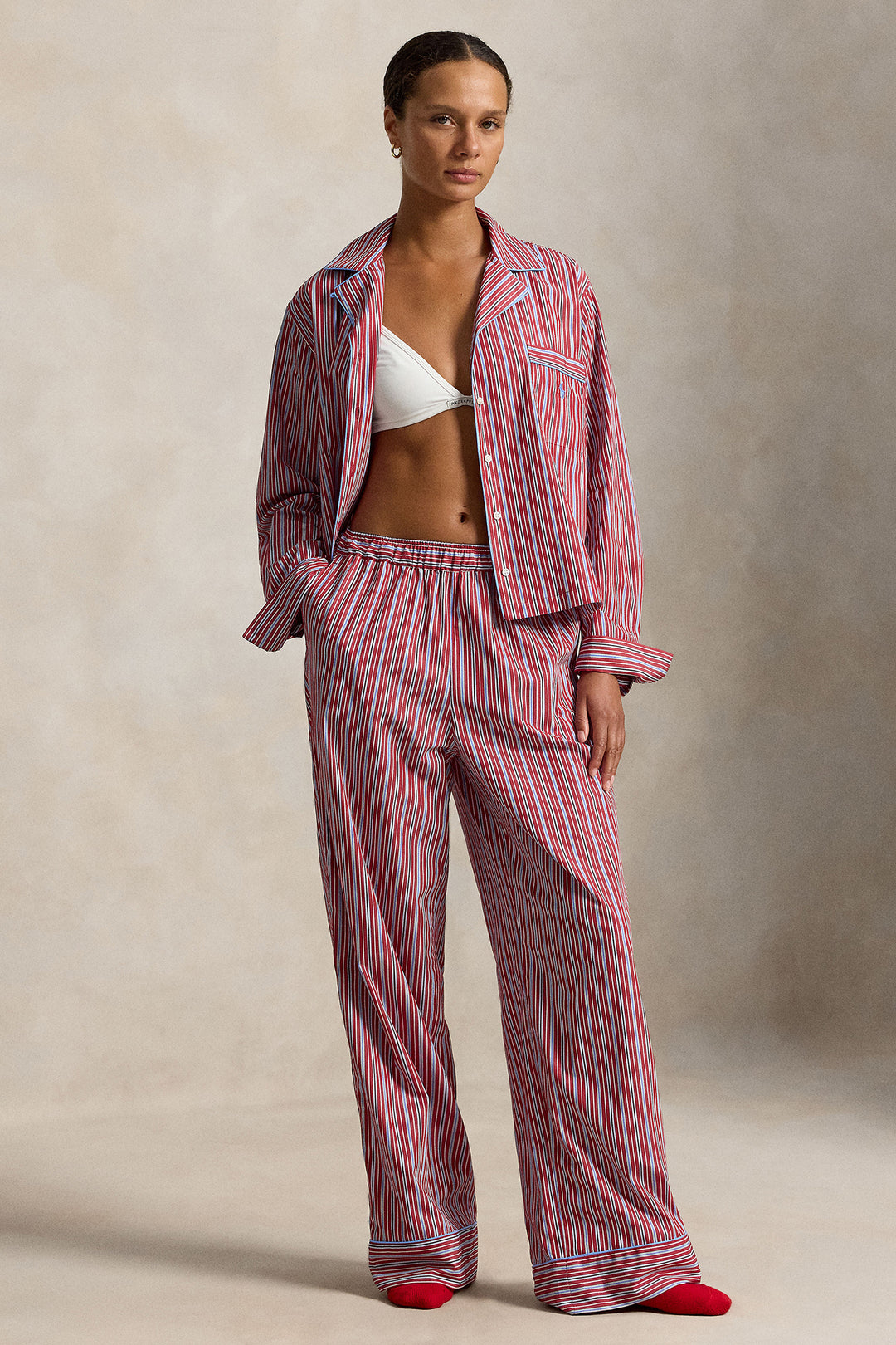woman wearing a red blue striped pajama set with blue piping trim. Buttoned top with notch collar and full length pant with elastic waistband. 