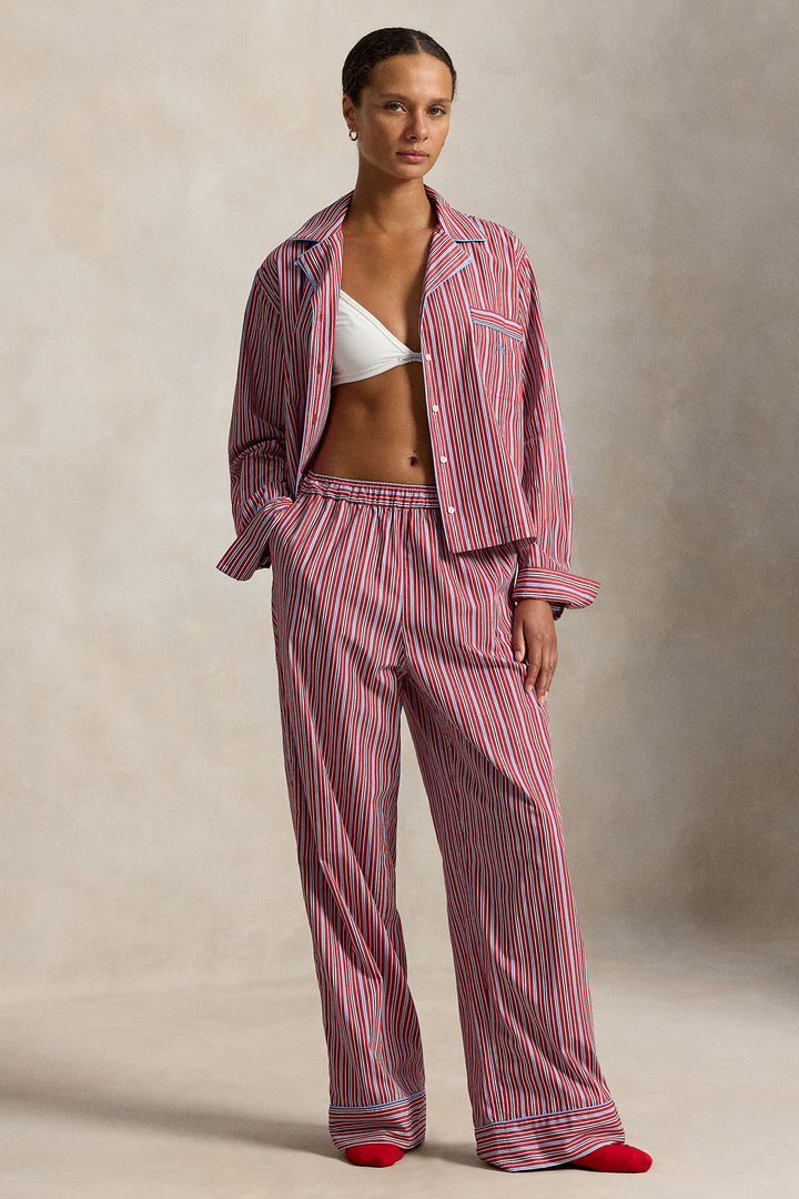 woman wearing a red blue striped pajama set with blue piping trim. Buttoned top with notch collar and full length pant with elastic waistband. 